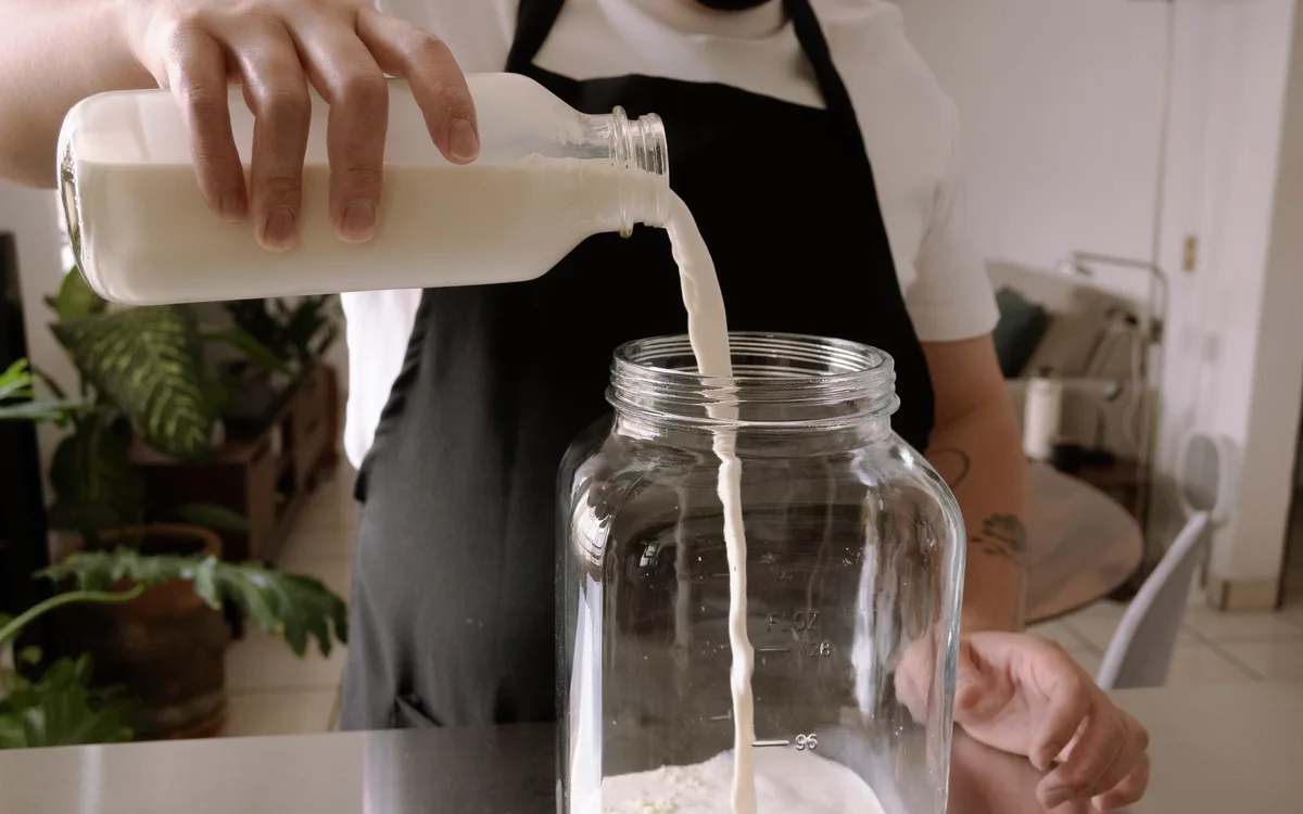 Mario vierte la leche fresca desde la botella al frasco de vidrio.